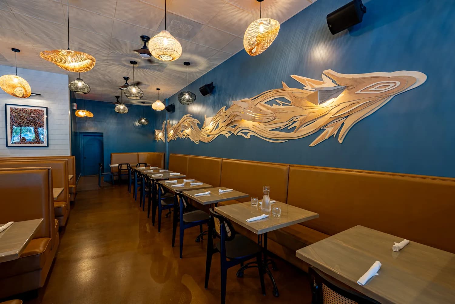 The Sweet Fish dining room with leather banquette booths, rattan pendant lights, and a carved wave wall sculpture.