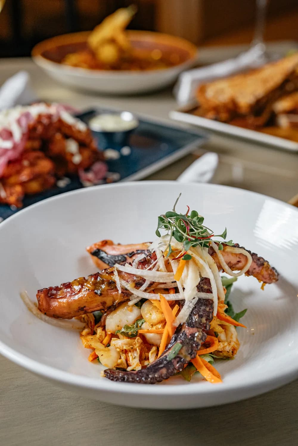 Charred grilled octopus with shaved fennel, carrot, and microgreens in a white bowl.