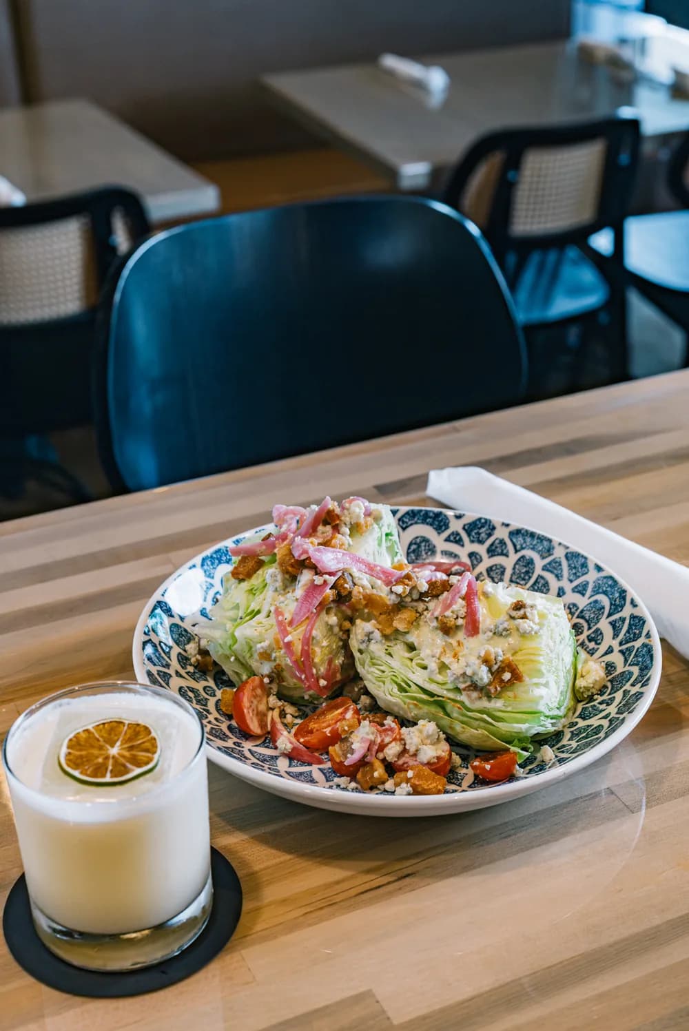 A wedge salad with blue cheese, cherry tomatoes, pickled red onion, and chicharrón on a patterned plate.